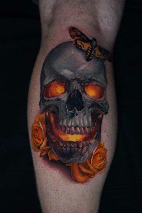 Colour skull with glowing eyes, a moth and orange roses on a calf.
