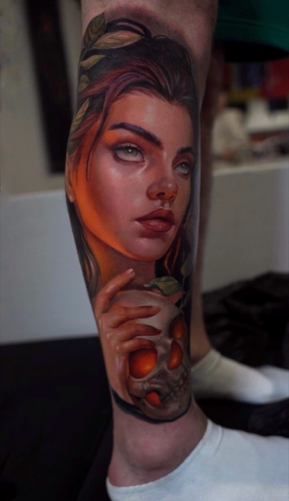 Woman with auburn hair holding a glowing golden skull, colour tattoo on a calf.